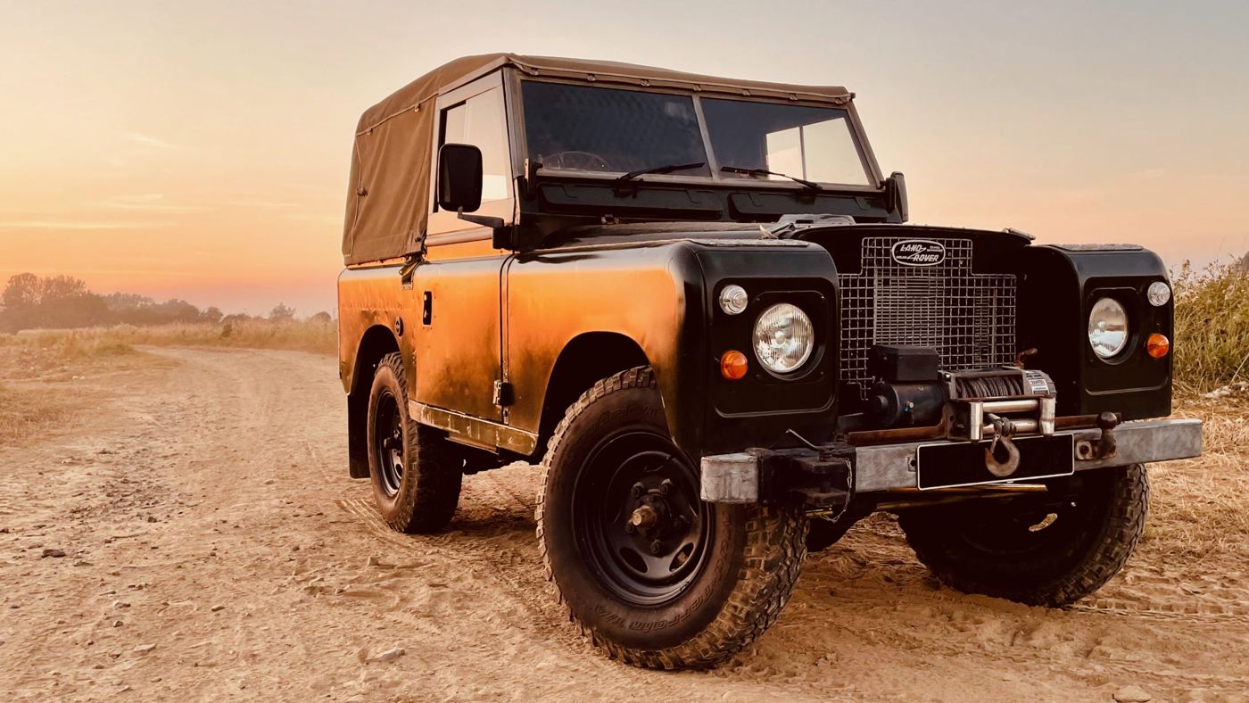 A classic Land Rover Series 88 with a canvas top at sunset